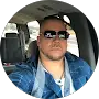 A person wearing sunglasses and a blue plaid shirt is sitting in the driver's seat of a vehicle.