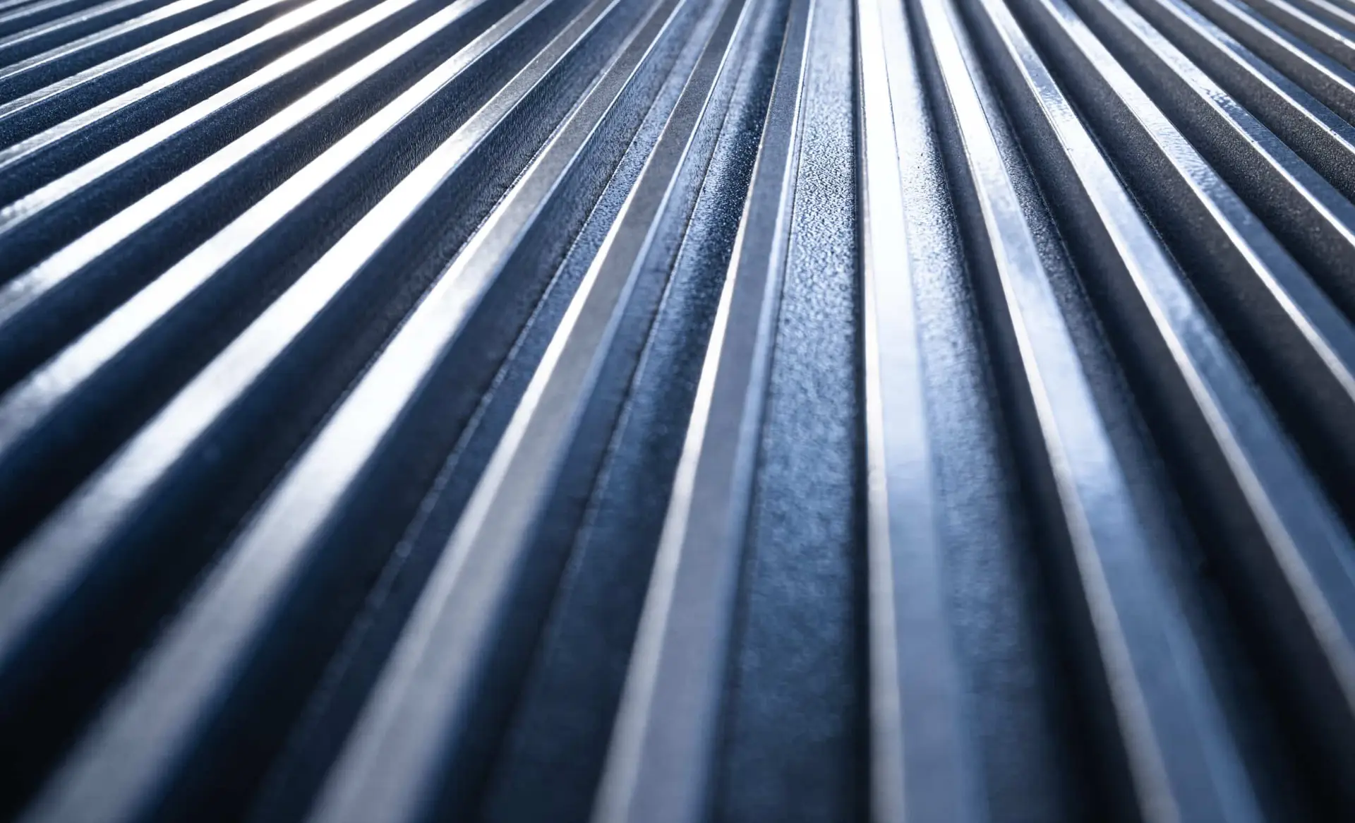 Close-up view of metallic parallel ridges or corrugated metal panels, photographed from a low angle with light and shadow emphasizing the texture.